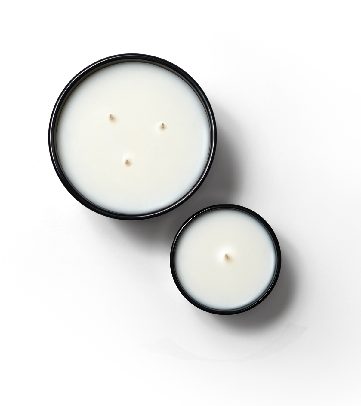 Editorial aerial shot of Standard and Magnum Candles. AMagnum is featured on the left with 3 wicks and standard is featured on the right with one wick. Both candles are against a neutral background.
